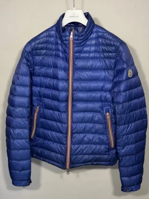 Daniel Down Jacket - Dunjacka från Moncler i en sällsynt blå färg. Jackan är i fint skick med endast en liten lagning (se bild 5), vilket inte är något man tänker på vid användning. Storlek 3 sitter som en M.