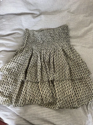 Mönstrad kortkjol från Sofie Schnoor - Kortkjol från Sofie Schnoor i mörkgröna och beige med smock i midjan och volangdetaljer. Kjolen har ett grafiskt mönster och är tillverkad i ett lätt och luftigt material, perfekt för varmare dagar.