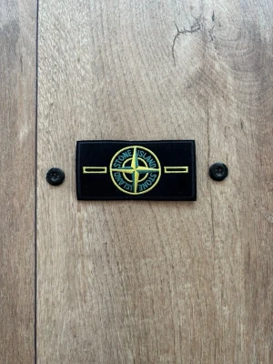 Stone Island Original Patch / Badge – Helt ny & oanvänd - Säljer en klassisk Stone Island-badge med tillhörande originalknappar, precis som visas i bilden. Patchen är helt ny, aldrig använd och i perfekt skick. Perfekt som reservdel till din Stone Island-jacka eller tröja. Klassisk gul/grön design. 