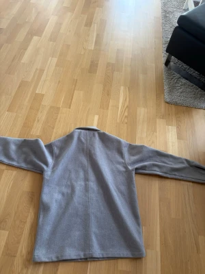 Ljusgrå overshirt med fickor - Snygg ljusgrå overshirt med klassisk krage och två stora bröstfickor. Rak passform och knäppning framtill med matchande knappar. Tillverkad i ett mjukt tyg som ger en clean och stilren look. Perfekt att slänga över en hoodie eller t-shirt.