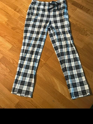Rutiga pyjamasbyxor från Kappahl - Oanvända flanellpyjamasbyxor från KappAhl. Mjuka och sköna med rutigt mönster i vitt, grått och svart. Resår och justerbara snören i midjan för bra passform. Perfekta för mysiga kvällar hemma
