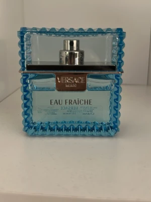 Versace Eau Fraîche parfym 50ml - Fräsch parfym från Versace, Eau Fraîche, i en snygg blå glasflaska med silverdetaljer. Flaskan har en rektangulär form med markerade kanter och genomskinligt blått glas som ger en lyxig känsla. Perfekt för dig som gillar eleganta och fräscha dofter.