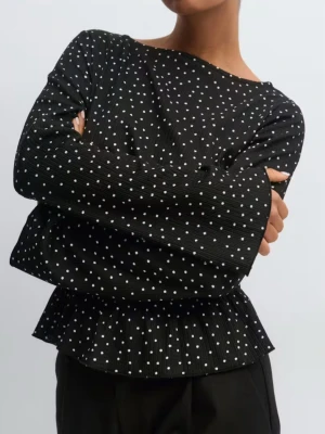 Svart prickig blus med volang - Trendig svart blus med vita prickar och smockad midja som ger en snygg siluett. Blusen har långa ärmar och volangkant nedtill för en extra detalj. Perfekt till både jeans och kjol för en cool look.
