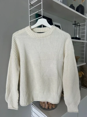 Krämvit chunky stickad tröja - Säljer en chunky stickad tröja i offwhite med bred ribbad kant vid hals, ärmslut och nederkant. Tröjan är i skönt material och är stickad i olika strukturer som. Perfekt för dig som gillar en avslappnad och trendig stil.