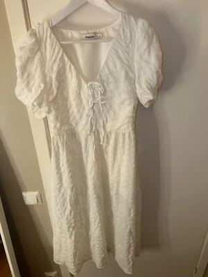 Vit klänning från Kappahl - Söt vit kortklänning från Kappahl med puffärmar och v-ringning. Klänningen har snörning framtill och är tillverkad i ett strukturerat tyg som ger en fin känsla. Perfekt för sommarens alla tillfällen! Aldrig använd.