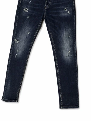 Mörkblå slitna skinny jeans - Säljer ett par mörkblå skinny jeans med slitningar och distressed detaljer på både fram- och baksida. Jeansen har klassisk femficksmodell och är tillverkade i stretchigt denimtyg för en bekväm passform. Perfekta för en avslappnad och trendig look.