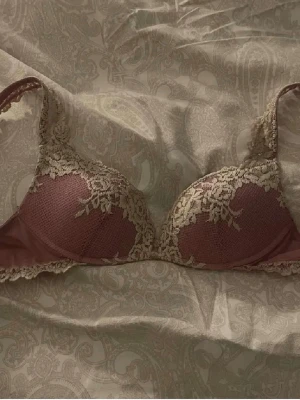 Rosa intimissimi push-up bh med spetsdetaljer - Snygg push-up bh i dammigt rosa med beige spetsdetaljer längs kanterna och axelbanden. Bh:n har vadderade kupor och vacker spets som ger en romantisk känsla. Perfekt för dig som gillar feminina underkläder. Köp direkt, inga prisförändringar. 