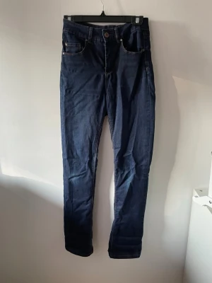 Mörkblå jeans med hög midja - Säljer ett par mörkblå jeans med hög midja och klassisk femficksdesign. Jeansen har smala ben och är sydda i stretchigt denimtyg för en bekväm passform. Perfekta till en avslappnad look och lätta att matcha med olika stilar.