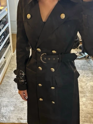 Svart trenchcoat med guldknappar - Svart kappa från Coventina Collection, använd en gång.