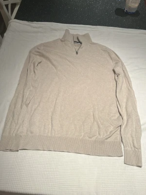 Beige halvzip-tröja Jack & Jones - Snygg beige långärmad tröja från Jack & Jones med halv dragkedja vid halsen. Tröjan har ribbade muddar och är tillverkad i mjukt material som känns skönt mot huden. Perfekt för lager-på-lager och enkel att matcha med jeans eller chinos.