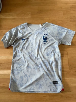 Frankrike Nike fotbollströja blåvit - Snygg fotbollströja från Nike i blåvitt med Frankrikes landslagsemblem och två stjärnor på bröstet. Tröjan har diskret mönster i tyget och korta ärmar. Perfekt för dig som älskar fotboll och vill stötta Les Bleus.