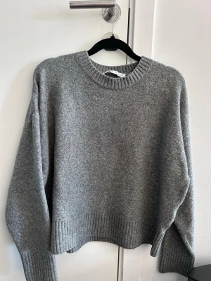 Grå stickad tröja från Zara - Mysig grå stickad tröja från Zara med rund halsringning och ribbade muddar vid ärmslut och nederkant. Tröjan har en avslappnad passform och är perfekt för kyliga dagar.