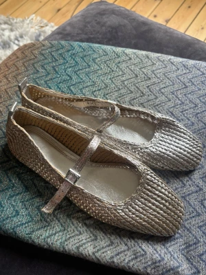 Ballerinaskor i silver  - Säljer ett par silvriga ballerinaskor från H&M med flätad struktur och justerbar rem över foten i Mary-Jane modell. Köpta förra sommaren, aldrig använda! 