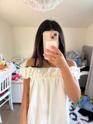 Vit offshoulder topp med volang - Säljer en söt vit offshoulder topp med bred volang runt axlarna. Toppen har en luftig och lös passform, perfekt för varma dagar. Tillverkad i ett mjukt bomullsliknande material och passar till jeans eller kjol.