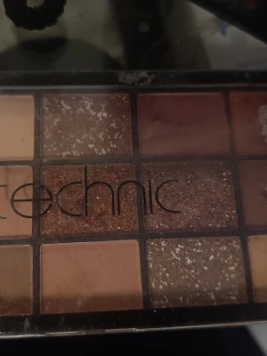 Technic ögonskuggspalett i varma toner - Palett med 12 ögonskuggor i varma nyanser som beige, brunt, koppar och guld. Innehåller både matta och skimrande skuggor, perfekt för att skapa olika looks. Skuggorna har en rektangulär form och paletten är kompakt och smidig att ta med.