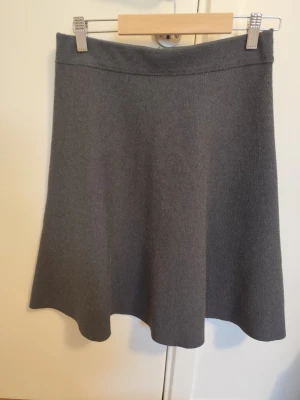 Grå A-linjeformad kjol - En stilren grå kjol i A-linjeform med enkel midja och mjukt fall. Kjolen är enfärgad och har en klassisk, tidlös look som passar till många olika outfits. Perfekt för dig som gillar minimalistisk stil och vill ha en mångsidig kjol i garderoben.