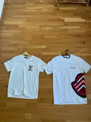 Två vita  t-shirts - Snygg vit t-shirt från  med klassisk -logga i brunt och svart på bröstet. T-shirten har rund hals och korta ärmar, perfekt för en clean och stilren look. Materialet ser ut att vara mjukt bomullstyg. Det två t shirt för ett pris den vita till höger är storlek M och den andra är storlek S