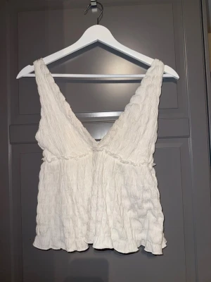Vit linnetopp med v-ringning - Säljer en vit linnetopp med djup v-ringning både fram och bak. Toppen har en lätt rynkad struktur och volangkant nedtill. Perfekt för varma dagar och enkel att styla med jeans eller kjol.