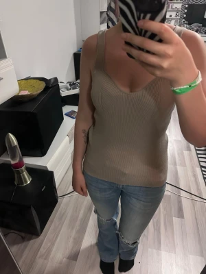 Beige ribbad linnetopp - Säljer en beige ribbad linnetopp med breda axelband och v-ringad urringning. Toppen har en figurnära passform och är tillverkad i ett mjukt, stretchigt material som känns skönt mot huden. Perfekt att styla med jeans eller kjol för en trendig look. Storlek M men skulle kunna passa en mindre L med 🌷pris går att diskutera 