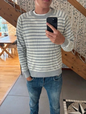 Gråvit randig tröja från SUN68 - Snygg gråvit randig tröja från SUN68 i mjukt material. Tröjan har rund halsringning, ribbade muddar vid ärmslut och nederkant samt en avslappnad passform. Perfekt för en casual och stilren look.