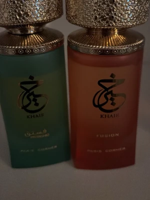 Khair Fusion parfym duo - Två exklusiva parfymer från Khair-serien av Paris Corner. Ena flaskan är grön och den andra är röd, båda med guldfärgade, mönstrade korkar och elegant design. Flaskorna har arabiska och engelska texter och ger en lyxig känsla till din parfymhylla.