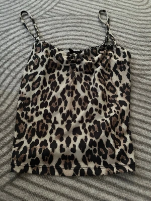 Leopardmönstrad linnetopp Gina Tricot - Snygg leopardmönstrad linnetopp från Gina Tricot i storlek XS. Toppen har tunna axelband och en liten rosett framtill. Perfekt för dig som vill sticka ut med ett djurmönster och gillar trendiga detaljer.