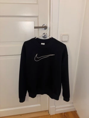 Svart Nike sweatshirt Dri-FIT XS - Säljer en svart sweatshirt från Nike i storlek XS. Tröjan har en klassisk rund halsringning och den ikoniska Nike-loggan i vitt på bröstet. Tillverkad i Dri-FIT-material som transporterar bort fukt och håller dig bekväm. Perfekt för en sportig och stilren look.