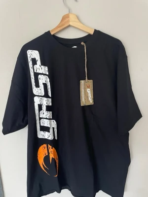 Svart oversized GASP t-shirt - Cool svart t-shirt från GASP med stort vitt tryck på både fram- och baksidan samt en orange logga framtill. Oversized passform och klassisk rund hals. Perfekt för dig som gillar streetwear och sportig stil.