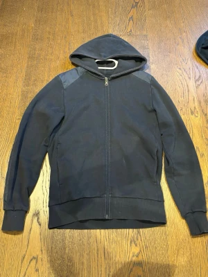 Mörkblå colmar zip hoodie med detaljer - Snygg mörkblå hoodie med dragkedja framtill och huva. Hoodien har coola detaljer i glansigt material på axlar och armbågar samt ribbade muddar. Perfekt för en avslappnad streetwear-look. Materialet är en mix av bomull och syntet.