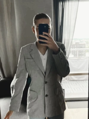 Ljusgrå figurformad kavaj - Snygg ljusgrå kavaj med två knappar framtill och stora fickor. Oversized passform och klassisk krage. Materialet ser ut att vara en blandning av bomull och polyester, vilket ger en mjuk och lätt struktur. Perfekt för en trendig och avslappnad look.