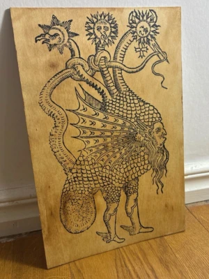 Hermetiskt tavla  - Unik träplatta med handritad illustration av ett mytologiskt monster. Motivet visar en varelse med fjäll, vingar, människoansikte, lejonben och tre huvuden på ormliknande halsar. Svart bläck på ljust trä. Perfekt som dekoration för dig som gillar fantasy och konst.