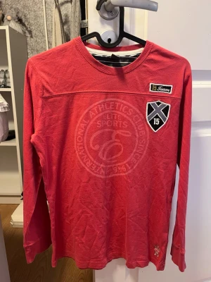 Röd långärmad tröja från Zara Kids - Cool röd långärmad tröja från Zara Kids med tryck och patchar framtill. Rund halsringning och mjukt bomullsmaterial. Perfekt för dig som gillar sportig stil och snygga detaljer.