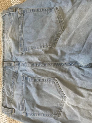 Ljusblå jeans från Nelly - Säljer ett par ljusblå jeans från Nelly med råa, fransiga kanter och klassiska bakfickor. Jeansen har en avslappnad passform och är gjorda i denim med synliga sömmar.  Perfekt för en avslappnad stil och ger en cool, avslappnad vibe.