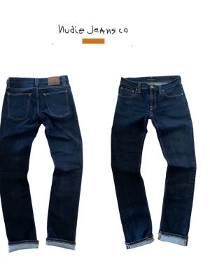 Mörkblå jeans från Nudie Jeans - Snygga mörkblå jeans från Nudie Jeans med klassisk femficksdesign och kontrastsömmar. Jeansen har raka ben och uppvikta benslut. Tillverkade i denim med en stilren look som passar till många outfits.