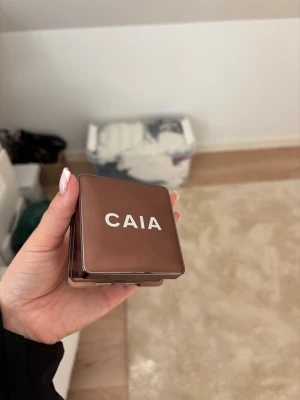CAIA Glow bronzer  - Säljer en bronzer från CAIA i en snygg brun metallask med spegel.  Perfekt för att skapa en solkysst look och definiera ansiktet. I färgen Monaco de bild för skicket 