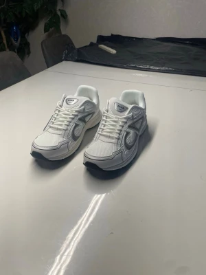 Vita sneakers med grå detaljer - Snygga vita sneakers med grå detaljer och svart sula. Skorna har en sportig design med mesh och syntetmaterial, samt tydliga sömmar och paneler på sidorna. Perfekta för dig som gillar en clean och modern look.