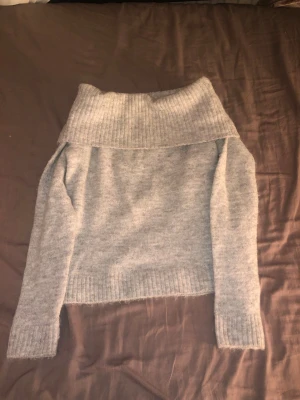 Ljusgrå off shoulder stickad tröja - Mysig ljusgrå stickad tröja med bred polokrage som kan bäras off shoulder. Tröjan har långa ärmar och ribbstickade muddar vid ärmslut och nederkant. Perfekt för kyliga dagar och enkel att matcha med jeans eller kjol.