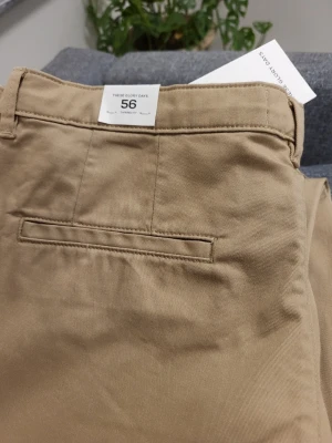 Beige chinos från These Glory Days - Snygga beige chinos från These Glory Days i storlek 56. Klassisk rak passform med bälteshällor, knappgylf och diskreta bakfickor. Tillverkade i mjukt bomullstyg som ger en clean och stilren look. Perfekta för en avslappnad men ändå uppklädd stil.