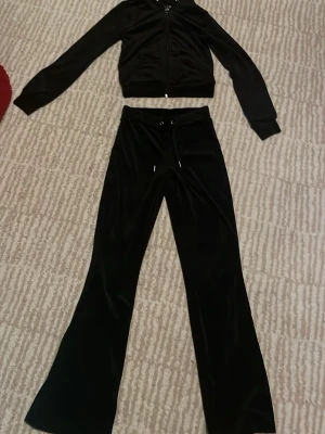Svart velour mjukisdress (set) - Säljer ett svart velour mjukisset med zip-hoodie och matchande byxor. Byxorna har dragsko i midjan och vida ben. Perfekt för mysiga dagar hemma eller en avslappnad vardagslook. Använd fåtal gånger, i mycket fint skick!