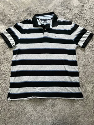 Tommy Hilfiger Randig Pikétröja Herr XL Custom Fit - Klassisk randig pikétröja från Tommy Hilfiger i grått, svart och blått. Snygg passform och ikonisk logga på bröstet.