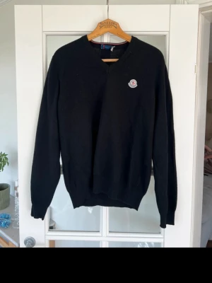 Svart Moncler tröja med logga - Snygg svart tröja från Moncler med rund halsringning och Moncler-logga på bröstet. Tröjan har en klassisk passform och ribbade muddar vid ärmslut och nederkant. Perfekt för dig som gillar stilrena och exklusiva plagg. Storlek L