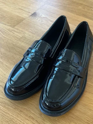 Svarta lackloafers  - Säljer ett par svarta loafers med de perfekta detaljerna och en lägre klack. Jätte snygga och helt oanvända eftersom jag har ett par identiska. Skorna är strl 41 men passar 40 då de är mindre i storleken ☺️