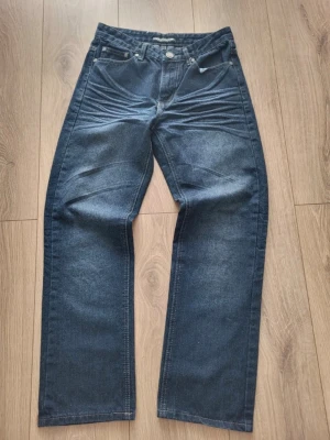 Mörkblå raka jeans med hög midja - Säljer ett par mörkblå jeans med raka ben och hög midja. Jeansen har klassiska fem fickor, silverfärgade knappar och subtila slitningar vid låren. Perfekta för en avslappnad och trendig look. Skriv vid frågor priset kan diskuteras 