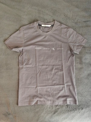 Calvin Klein tshirt - Stilren grå t-shirt från Calvin Klein med diskret logga och text framtill. Mjuk och skön 100%. Storlek L enligt lappen men skulle mer säga slim M. Färgen är lite svår att beskriva men är en mjukare variant av brun, inte bajs brun men en mer "earth" eller "naturlig" variant. Har använt den max 2 gånger och den har bara legat i garderoben ett bra tag. Skriv till mig för fler bilder, info eller prisförslag! 😎