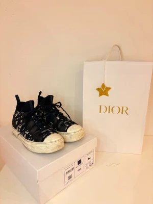 Dior Oblique mörkblå sneakers - Snygga Dior Oblique sneakers i mörkblå och vitt med monogrammönster. Skorna har svarta snören, vit sula och detaljer i textil och gummi. Klassisk siluett med högt skaft och ribbad kant vid ankeln. Äkta, äktensbevis ligger i lådan som ni ser, samt nya skosnören, köpta i puerto Banús för nått årsen bara, väldigt fint skick, använda nåra gånger