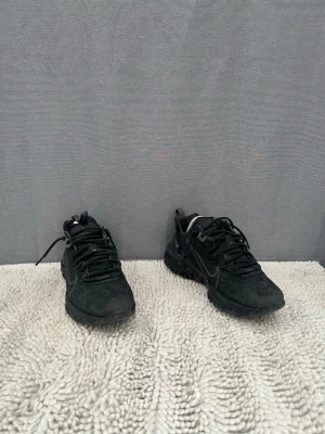 Svarta Nike react sneakers - Säljer ett par sköna svarta Nike react sneakers. Svarta snören och en robust sula med mönster för bra grepp. Swoosh-loggan syns på sidan och designen är sportig och modern.