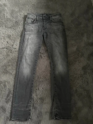 Grå slim fit jeans med tvättade detaljer - Snygga grå slim fit jeans med tvättade detaljer och klassisk femficksmodell. Jeansen har normal midja och raka ben. Materialet är troligtvis bomull med stretch för extra komfort. Perfekta för en avslappnad och trendig look.