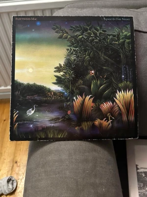 Fleetwood Mac - Tango In The Night - Säljer en LP-skiva med albumet 'Tango In The Night' av Fleetwood Mac. Omslaget har ett färgstarkt motiv med natur och fåglar på framsidan och ett foto av bandet på baksidan. Perfekt för dig som gillar klassisk rock och samlar på vinyl.