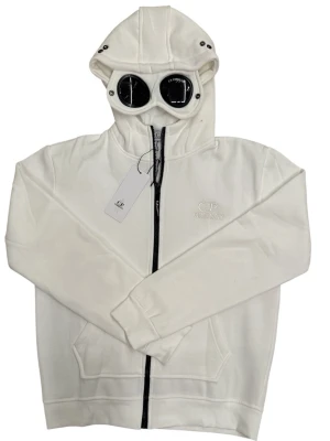 Vit hoodie från C.P. Company- storlek L( helt ny ) - Snygg vit hoodie från C.P. Company med dragkedja framtill och klassisk huva med svarta detaljer. Hoodien har två stora fickor framtill och diskret logga broderad på bröstet. Perfekt för en clean och stilren look. Den är liten är i storlek, egentligen är den storlek L fast den sitter som storlek M. Ny med tags