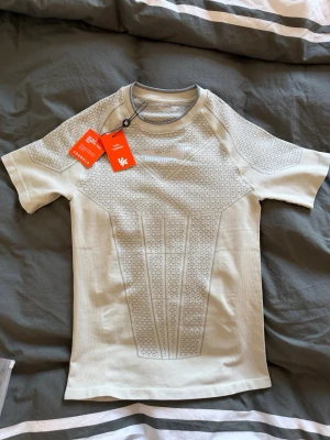 Youngla compression  - Säljer en off white , tight kompressionströja med korta ärmar och unikt geometriskt mönster. Tröjan har rund halsringning och är tillverkad i ett stretchigt funktionsmaterial som andas, perfekt för träning och sport.